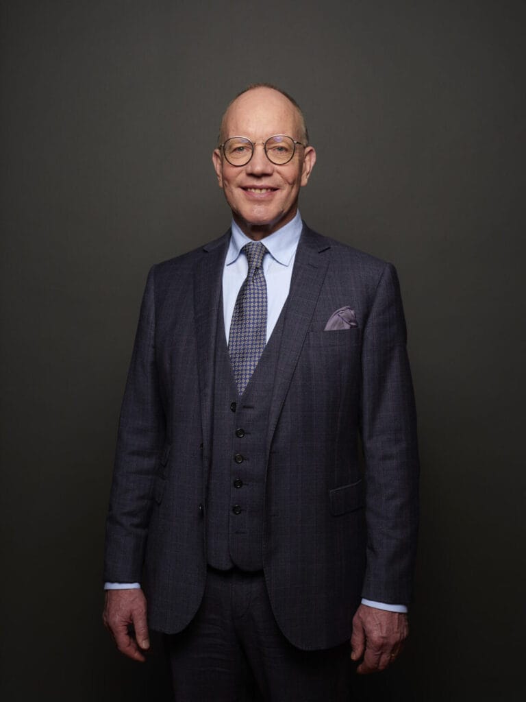 Mann im Anzug vor grauem Hintergrund lächelt